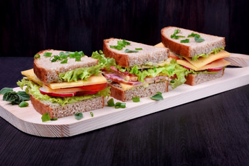 Sandwiches assortment on a wooden board against the dark background