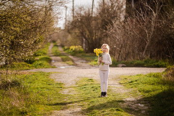 cute blonde happy little girl with yellow daffodils in the spring country