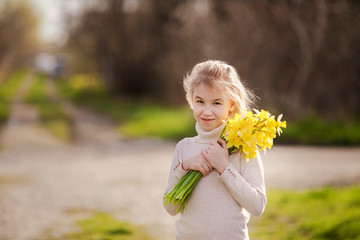 cute blonde happy little girl with yellow daffodils in the spring country