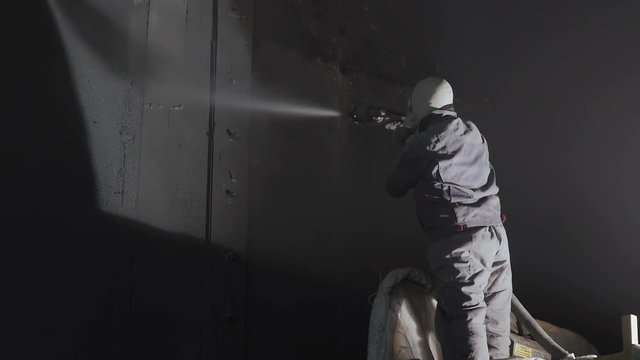 Industrial worker sprays polyurea to the concrete surface with a pressure gun. Industrial process of waterproofing with polyurea. A man in a protective form and respirator.