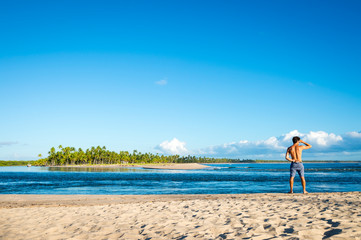 Bright scenic view of a rustic beach on a remote island off the coast of Bahia, Brazil with a solitary figure looking out at the horizon
