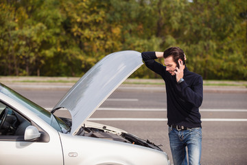 Handsome young man calling for assistance with his car broken down by the roadside
