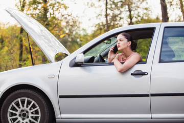 Young woman calling in evacuation service. Her car broke down on the road.