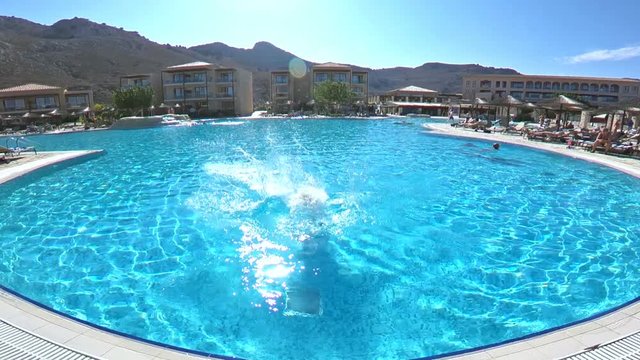 Young slender woman jumping into the pool and swimming under the water in summer sunny day. Underwater view. Slow motion.