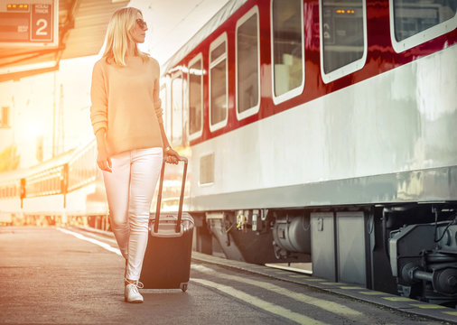 Woman With Her Luggage Go To Red Train Of Rail Station Under Sun Light At Sunny Day.