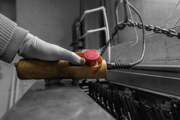 Man operating a control for an indoor crane hoist in a factory workshop with selective colour