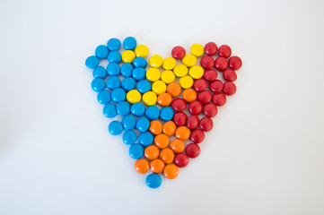 multicolored round candies dragees laid out in the shape of a heart on a white background