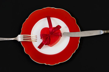 Red heart with a ribbon on a red plate.