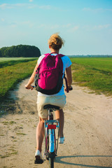 Fototapeta premium Young beautiful woman rides on a bicycle in the summertime on the green fields background