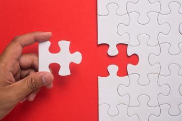 Close up of hand placing the last jigsaw puzzle piece on red background. Business and team work concept.