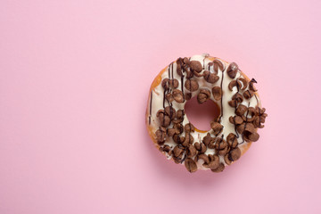 Fresh chocolate donut or doughnut decorated wit chocolate cereal on pink pastel table top