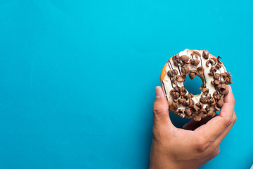 Hand holding delicious glazed doughnuts with choclate cereal topping on color background