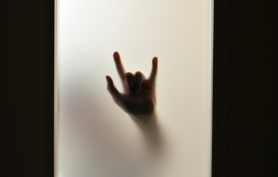 Hand showing devil's horns through frosted glass