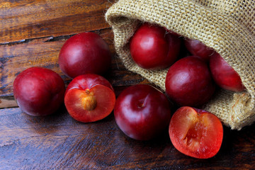 raw and fresh organic plums inside rustic fabric bag on wooden table