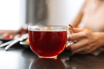 Cropped photo of european woman sitting at table in flat, with hot tea in glass