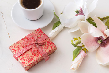 box with a bow, a Cup of black coffee, Magnolia flowers on a white table