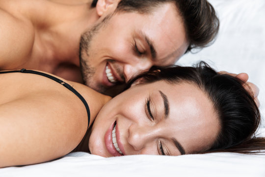 Portrait of european couple man and woman smiling, while lying in bed at home or hotel apartment