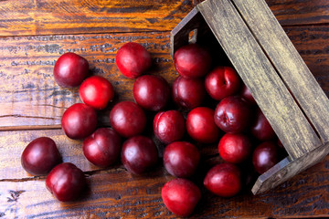 raw and fresh organic plums inside rustic fabric wooden box on rustic table