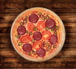 Isolated image of a Devil Pizza with tomatoes and jalapeno on a wooden background