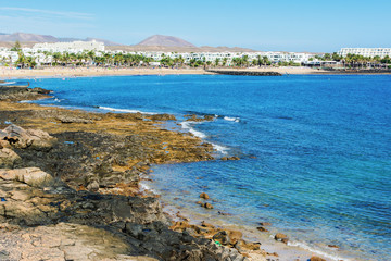 Fototapeta na wymiar Golden sand and volcanic rocks at Las Cucharas beach, Lanzarote, Canary islands. VIew of the sea, coast and rocks, selective focus