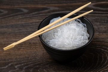Rise noodles in black bowl on wooden background