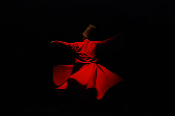 Whirling dervish in red garment on black background