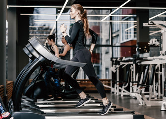 Fototapeta na wymiar The athletic girl dressed in a black sportswear running on the treadmill in the modern gym