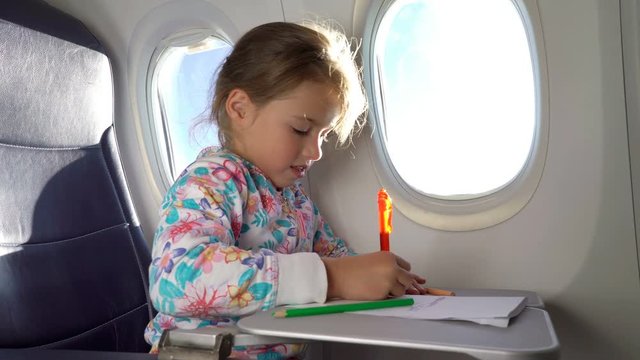 A little cute girl traveling by an airplane and drawing a picture with colorful pencils.