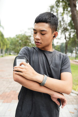 Fit Asian man setting program in smartphone on his arm before running outdoors