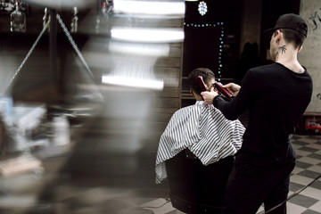 Men's style. The fashion barber makes a stylish hairstyle for a black-haired man sitting in the armchair in the stylish barbershop