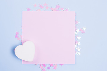 Pastel pink blank card mockup and white wooden heart on pastel blue background with scattered pink glitter stars. Place for your text. Gbar style.