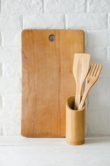 Wooden or bamboo cutlery and cutting board in interior of white kitchen.