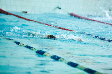 Children swimming freestyle at swimming lesson. Elementary school children within swimming skills lesson. School children are learning to swim. Children swimming competition in indoor pool