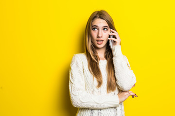 Portrait of a smiling young woman talking on mobile phone dressed in sweater standing isolated over yellow background