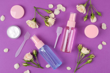 cosmetics for face and body in pink bottles with fresh roses on a bright purple background. spa. top view