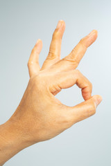 Woman's left hand symbol meaning " OK " on grey  background, Close up & Macro shot, Selective focus, Asian body skin part, Symbol, Gesturing, Body Language Concept