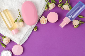 Obraz na płótnie Canvas cosmetics for face and body in pink bottles with fresh roses on a bright purple background. cream and lotion, sea salt and soap. spa. view from above. space for text