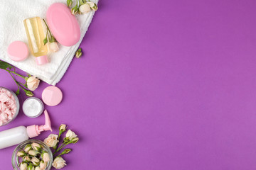 cosmetics for face and body in pink bottles with fresh roses on a bright purple background. cream and lotion, sea salt and soap. spa. view from above. space for text