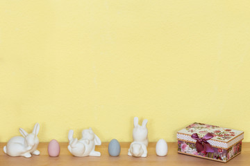 Fototapeta na wymiar Drei weiße Hasen und drei Ostereier mit einem Geschenk auf einem Holzboden