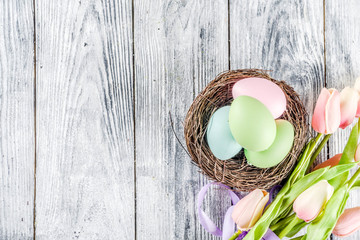 Pastel Easter background with tulip flowers and colorful painted Easter eggs. Top view, rustic white wooden table. Background for greeting card. Copy space for text