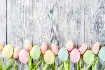 Pastel Easter background with tulip flowers and colorful painted Easter eggs. Top view, rustic white wooden table. Background for greeting card. Copy space for text
