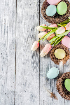 Pastel Easter background with tulip flowers and colorful painted Easter eggs. Top view, rustic white wooden table. Background for greeting card. Copy space for text
