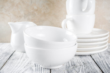 Assortment stack clean empty new white kitchen utensils, plates, bowls, cups mugs. On a white concrete background