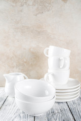 Assortment stack clean empty new white kitchen utensils, plates, bowls, cups mugs. On a white concrete background