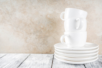 Assortment stack clean empty new white kitchen utensils, plates, bowls, cups mugs. On a white concrete background