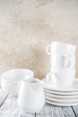 Assortment stack clean empty new white kitchen utensils, plates, bowls, cups mugs. On a white concrete background