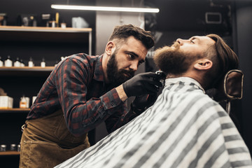 Hipster young good looking man visiting barber shop. Trendy and stylish beard styling and cut.