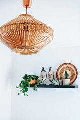 A trendy bamboo lamp hanging in front of a shelf with African art decoration and various house plants and cacti.