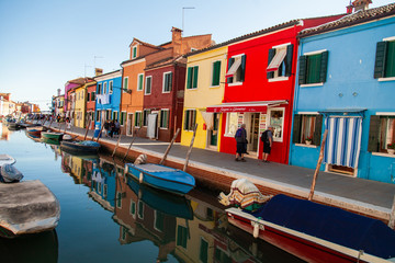 Fototapeta na wymiar Burano island picturesque street with small colorful houses, smal water canal with beautiful reflections and boats, Venice Italy 
