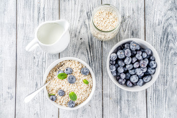 Healthy cereal and milk breakfast concept, dry oats in small bowl, with milk and fresh blueberry,...